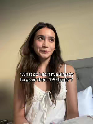 A young woman with long brown hair is looking up and slightly to her right. She is wearing a white top and is sitting on a bed, with a bed head in the background. The caption reads, "What do I do if I've already forgiven them 490 times?"