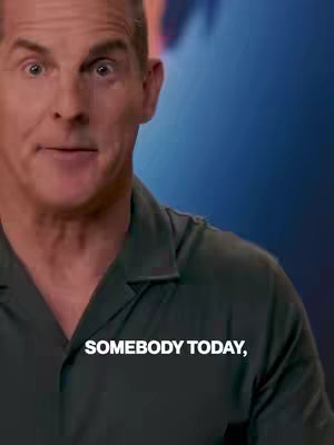 A man looks directly at the camera with a slightly surprised expression. Text overlayed on the image reads "SOMEBODY TODAY," in a white, bold font. The background is out of focus with shades of blue and purple.