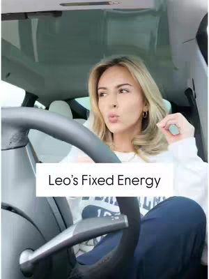 A woman is seated in the driver's seat of a car, looking towards the camera. Overlay text at the bottom center indicates a title. The interior of the car is visible, with a steering wheel and the windshield. The woman is wearing a white top and the background seems blurry
