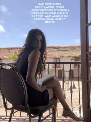 A woman sits on a chair on a balcony, holding a book. The background shows a building with a blue sky. Text overlayed on the top of the image.