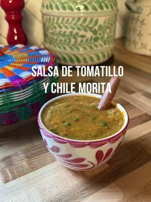 The cover image showcases a vibrant Mexican salsa in a decorative bowl. The bowl, with a design of pink and white, is placed on a wooden surface. The salsa presents a textured, reddish-brown color. A wooden spoon rests in the salsa. In the background, a colorful basket, a spice grinder, and a patterned jar contribute to the setting. The text overlay, provides the title of the dish.