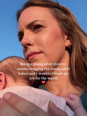 A woman with brown hair holds a baby close to her chest, with the baby's head visible. The woman looks slightly upward, bathed in soft sunlight, while text overlays describe the scene.