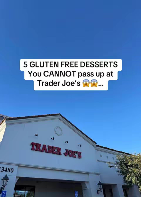 The image shows the exterior of a Trader Joe's store under a clear blue sky. The store's sign, 'TRADER JOE'S,' is prominently displayed in a red font. Overlayed on the image is a white rectangle containing the text: '5 GLUTEN FREE DESSERTS You CANNOT pass up at Trader Joe's 😳😳...'.