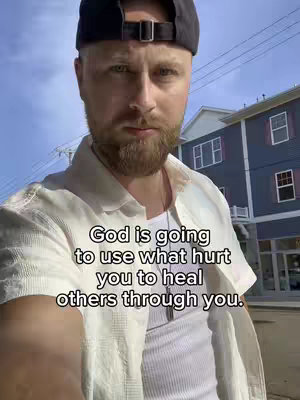 A selfie-style shot with a man in the foreground and a building in the background. The man is wearing a black cap and a white shirt, with text overlaying the image.