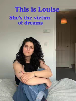 A woman with dark curly hair sits on a bed with neutral-toned bedding, looking directly at the camera with a serious expression. She is wearing a black top and blue jeans. Text in a blue font is superimposed on the image, stating 'This is Louise She's the victim of dreams'. The background is blurred, suggesting an indoor setting with a door and a ceiling light.