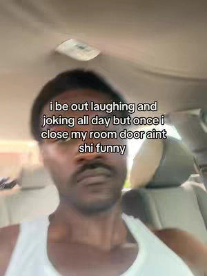 A man in the front seat of a car, with a white tank top, looking directly at the camera. Text is overlaid on the image.