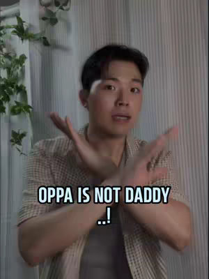 A man is positioned in the frame gesturing with his arms and hands. Overlayed on the image is text that reads, "OPPA IS NOT DADDY!" The background consists of vertical blinds or panels and some greenery on the left side.