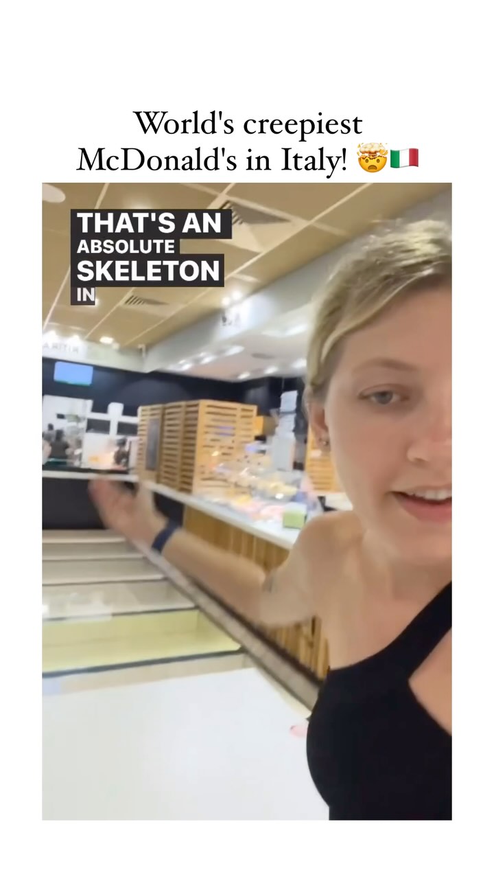 The cover image shows a selfie-style shot taken inside a McDonald's. The creator, a woman with blonde hair and a black top, is partially visible on the right side of the frame, gesturing with her left hand toward the interior of the McDonald's. The background shows the inside of the restaurant, with counters, service areas, and possibly other customers.
