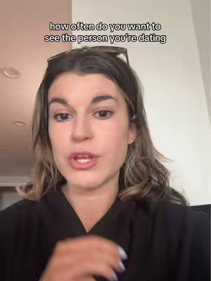 A woman with long, wavy brown hair is the central focus in a vertical frame. She wears a black top and has sunglasses perched on her head. The background is plain, and a text overlay at the top asks, "how often do you want to see the person you're dating."