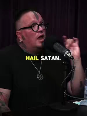 A man with tattoos and glasses speaks into a microphone with the text 'HAIL SATAN' overlaid.