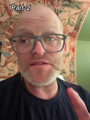 A middle-aged man with short, light-colored hair and a beard is centered in a selfie-style shot. He wears large, rectangular glasses and a black t-shirt. The background includes a patterned tapestry and part of a green wall. The text, 'Part-2,' is added to the top left corner of the image.