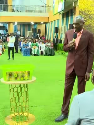 The cover image features a religious leader speaking into a microphone. He is dressed in a suit and tie and stands in front of a crowd. A green basket sits on a stand in the foreground. The setting appears to be a church or event hall, with individuals seated in the background.