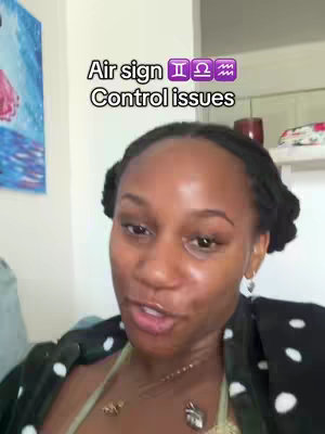 A selfie style video featuring a woman in front of a blurred background. She's wearing a black top with white polka dots, and her hair is styled in small buns on top of her head. The foreground shows a close-up view with text overlayed at the top of the image, stating a topic and symbol.
