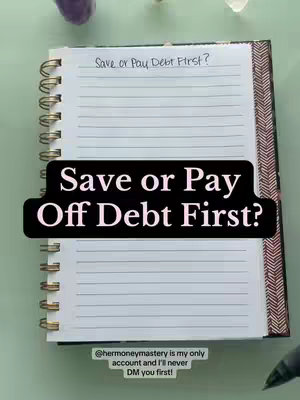 An open notebook with lined pages is the central focus, placed on a light green surface. The notebook has a metallic spiral binding on the left and a patterned cover. A dark rectangular text overlay, with white text, that reads, "Save or Pay Off Debt First?" is on the notebook pages. In the upper left portion of the image is a purple crystal formation, and scattered objects are present around the notebook, while in the lower right corner a pen is slightly visible.