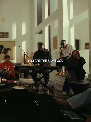 A group of musicians is performing in a well-lit, modern-style room. The image is a vertical shot, with the performers in the center and the text overlay at the bottom. The color palette is warm with neutral tones.