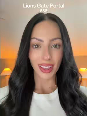 A woman with long black hair and fair skin is centered in the frame, smiling with her mouth slightly open. Above her, text reads 'Lions Gate Portal 888' in a white sans-serif font. The background is blurred, suggesting an interior with some yellow-toned lighting coming from lamps out of focus.
