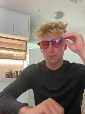 The cover image shows a young man with blond hair wearing dark sunglasses. He is holding the glasses and appears to be smiling. The background suggests a kitchen or living area, with cabinets and shelves visible. The lighting seems to be natural, and the overall composition focuses on the man's face and upper body.