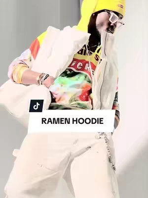 A person in a colorful hoodie and white pants stands against a white background. Text that reads 'RAMEN HOODIE' is over a black TikTok logo.