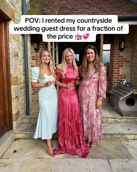 Three women stand outside a stone building. They are wearing dresses and smiling. Text in a bubble says "POV: I rented my countryside wedding guest dress for a fraction of the price".