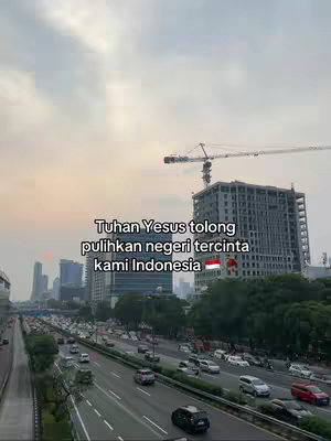 The cover image captures a wide cityscape with a cloudy sky, a highway filled with cars, and several high-rise buildings. In the foreground, a busy highway is visible. The sky is overcast. The text overlay reads: "Tuhan Yes us tolong pulihkan negeri tercinta kami Indonesia".