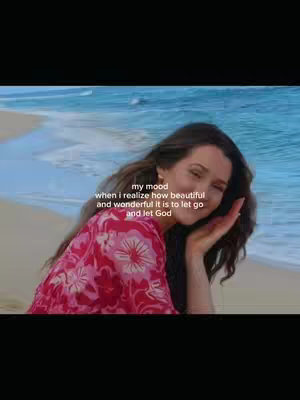 A woman with long, dark hair is featured in a selfie-style shot on a beach. The background is a blurred view of the ocean and sky. The image is softly lit with a warm color palette. The woman is wearing a vibrant, floral-patterned top, and her hand is gently touching her face. Text overlayed in the center reads, “my mood when i realize how beautiful and wonderful it is to let go and let God.”