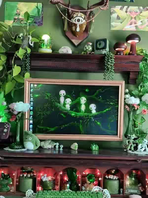 A cozy, whimsical gaming setup with a green aesthetic. The focal point is a computer monitor displaying a scene from a nature-themed animation. The setup includes fairy lights, plants, and themed decor.