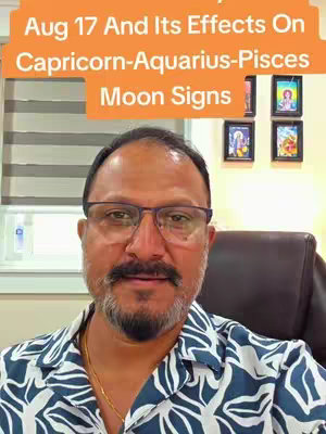 A man with glasses and a beard is centered. He is wearing a patterned shirt and golden necklace. Above him is a peach-colored banner with text. The background contains a window with blinds and pictures on the wall.