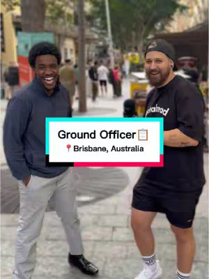 Two men stand in a city location, one smiling broadly while the other wears a serious expression, with a text overlay reading 'Ground Officer Brisbane, Australia'.