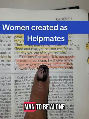 The image is a screenshot of a Bible passage open to Genesis 2 with text overlay in a blue box that says "women created as helpmates" over the words of the bible and a finger holding position with a manicured nail.