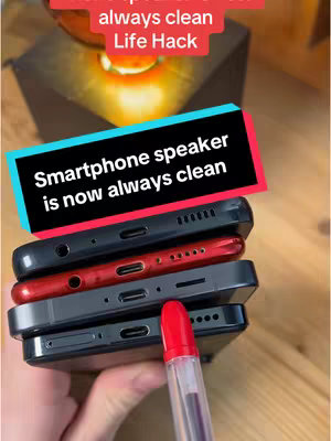 The image shows a stack of four smartphones, with their backs facing the viewer. The phones are in different colors: black, dark red, and two shades of gray. A red pen is held close to the phones, with its tip pointing towards their speaker holes.