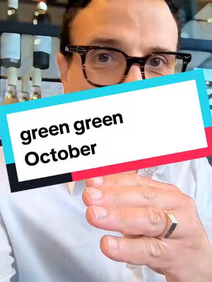 A person with glasses is in the image. Text overlayed in a white box with a red and turquoise accent reads "green green October". The person is looking at the camera and holding their hand up in a gesture.