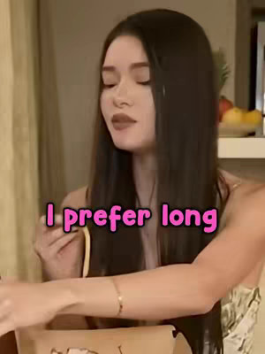 A woman with long, dark hair is the central focus. She is holding a yellow item in her hand, wearing a light-colored top and a gold bracelet. A pink text overlay stating 'I prefer long' is superimposed on the image.
