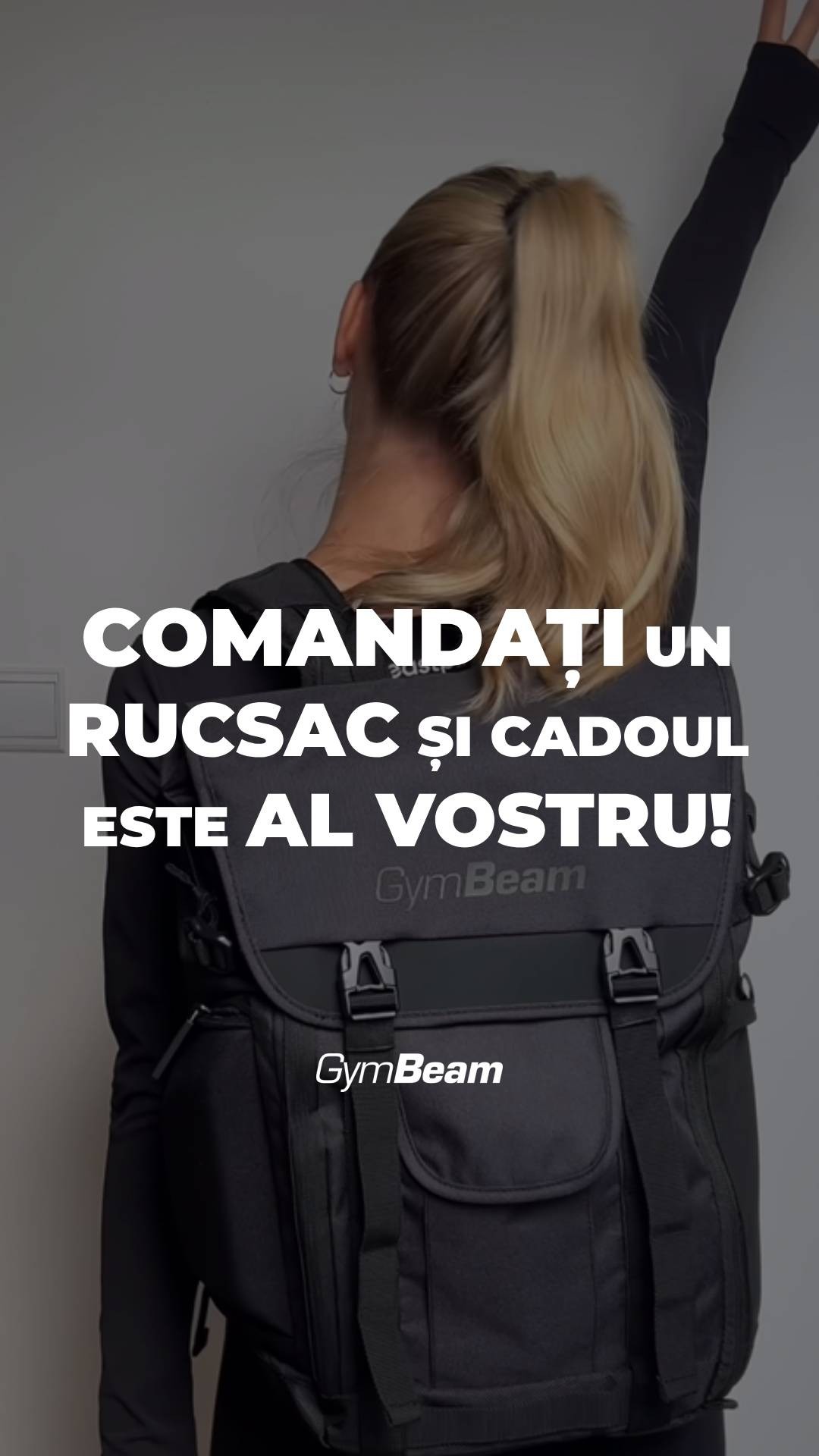 A portrait shot features a woman from the back, with her blonde hair pulled up in a high ponytail. She's wearing a black long-sleeve shirt and is seen from the mid-torso up. She is facing a gray wall, with her arm raised. In the foreground, a black backpack dominates the view. Bold white text overlays the image, and the GymBeam logo appears as well.