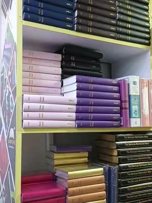 Image of bookshelves filled with books of varying colors and sizes. The shelves are arranged vertically and horizontally, dividing the space. The books on the shelves comprise different shades of purple, pink, gold, blue, and black. The books are neatly stacked on the shelves.