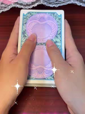Two hands holding a deck of tarot cards. The cards have a purple design on their back, and the background is a dark wooden surface with some sparkly animations.