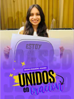 A young woman with long dark hair is smiling for the camera, holding up a sign with the words "Estoy Agradecido" and a purple background with the words "Unidos en Oracion". Behind here there is a golden color curtain.