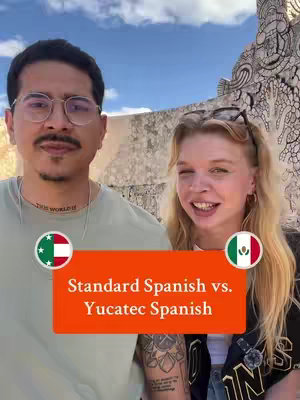 The image features a man and woman in a selfie with a historical background. The man has glasses and a tattoo on his arm, and the woman is smiling. Overlay text in an orange box reads “Standard Spanish vs. Yucatec Spanish”.