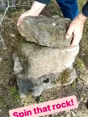 The image shows a duo of large rocks arranged in the outdoors. The top rock is being held by two hands, likely the person filming. A pink text box with the words 'Spin that rock!' is at the bottom.