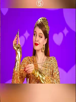 The cover image shows a woman posing in an elaborate, golden outfit, holding a lipstick. She wears a golden crown and large earrings. The background is a gradient of purple and white hearts, with a white square in the upper center, displaying the number 5.