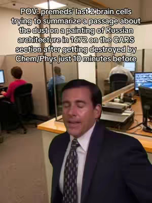 The image shows a medium shot of a man with brown hair wearing a black suit and a patterned tie. He is positioned in the foreground with his eyes closed and his mouth slightly open, as if he is speaking or concentrating. Behind him, a blurred office environment includes other people, computer screens, and office cubicles or partitions, creating a sense of a busy work or study atmosphere. Text in the upper portion of the image overlays the scene, adding context to the image.