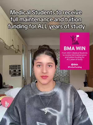 A young woman with dark hair looks directly at the camera, centered in the frame. She wears a gray and white patterned sweater and a delicate necklace. Behind her is a cozy setting. A pink square graphic with the text 'BMA WIN' anchors the right of the frame. The background includes cabinets, a window, and soft lighting. The overall composition is simple, direct, and informative.