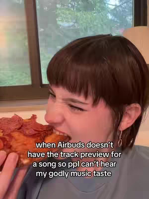 A woman with short brown hair is biting into a large slice of pizza, her expression is contorted as she chews. Text overlayed on the image reflects a humorous take on a music-listening scenario.