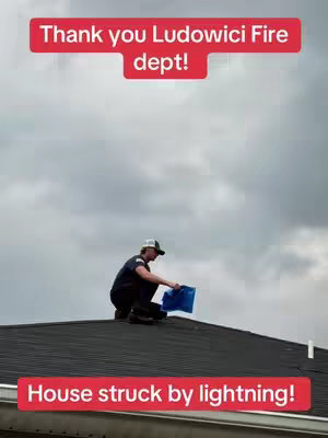 A man in a baseball cap and dark uniform is kneeling on a rooftop, holding a blue container, presumably assessing damage. The image is taken from a low angle, looking up at the roof against a cloudy sky. Text overlays announce 'Thank you Ludowici Fire dept!' and 'House struck by lightning!'.
