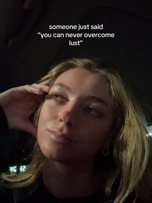 A selfie-style shot featuring a young woman. She is fair-skinned with light brown hair and is looking towards the right of the frame with a slight smile. Her left hand is raised, touching her temple, as if in thought. The background appears to be the inside of a dimly lit vehicle. Text overlayed at the top reads, 'someone just said "you can never overcome lust." The overall tone is contemplative.