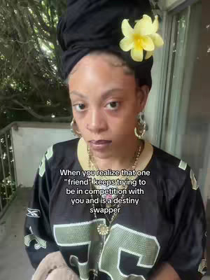 A woman with fair skin, wearing a black headscarf and a New Orleans Saints jersey, gazes directly at the camera with a somewhat serious expression. A yellow flower is tucked into her headscarf. Overlay text partially covers the bottom, indicating the video's theme of betrayal.
