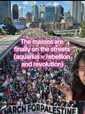 The cover image shows a crowd of people marching in a city. The crowd is dense, with many holding signs. In the foreground, the creator of the video is taking a selfie, and their face is visible, along with a peace sign. Text in a pink gradient is overlaid on the crowd in the middle area, explaining the image's context. Several tall buildings form a cityscape in the background. The overall tone is one of social activism.