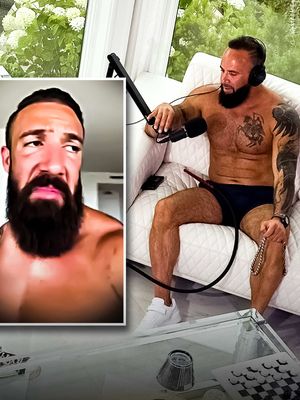 The image shows a man in a relaxed setting, likely for a podcast or interview. He is shirtless, wearing dark blue shorts and white sneakers, seated on a white couch with a microphone and headphones, in front of a window. A smaller inset image to the left shows a close-up of his face, with a concerned expression. There's a coffee table with objects like a hookah and a chess set.