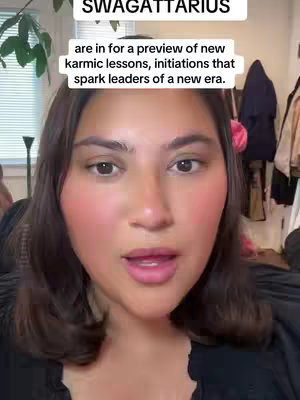 A woman with brown hair and makeup is centered in the frame, speaking with a casual expression. Text overlays at the top describe the video's astrological content. The background hints at a home setting.