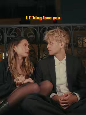 A cover image featuring a couple, a man and a woman, gazing at each other with expressions of contemplation. They are seated and framed against a background of dark, decorative metalwork. The lighting is dim, adding a sense of intimacy, with text overlayed on the upper part of the image, and it seems to have been enhanced with a filter.