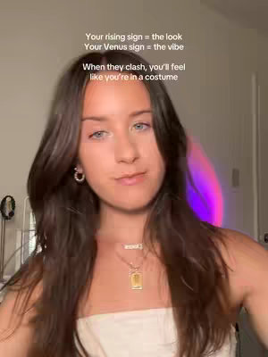 A young woman with long, dark brown hair and blue eyes looks directly at the camera. Above her head, text in white font provides context. The background includes a soft, blurred purple light. She's wearing small hoop earrings and a necklace with a gold pendant. The composition focuses on her face and upper body.